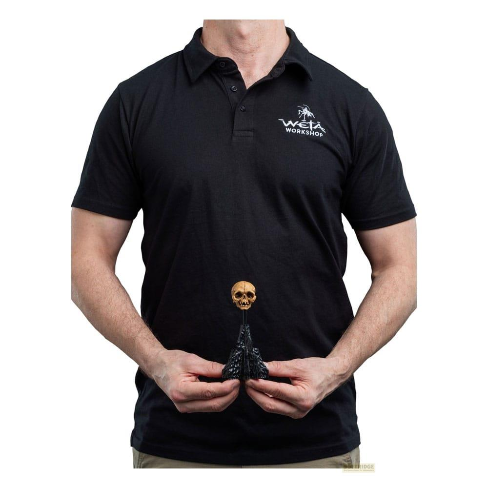 Ein Mann in schwarzem Polohemd hält ein kleines Totenkopf-Objekt mit schwarzem Sockel.