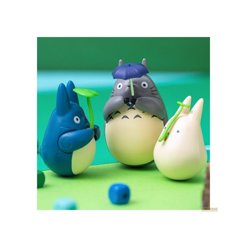 Trois figurines Totoro sur une surface verte. Une bleue tient une feuille. Le Totoro du milieu tient un parapluie bleu.