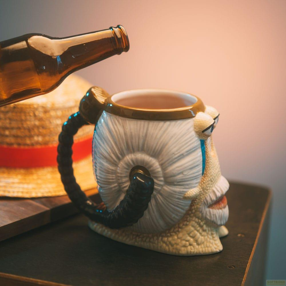 Eine braune Flasche neigt sich über eine Schnecken-Tasse und einen Strohhut.