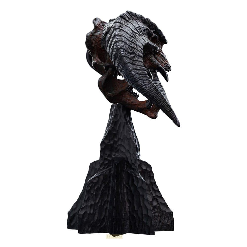 Una escultura oscura y texturizada de una calavera monstruosa con cuernos grandes sobre una base tallada.