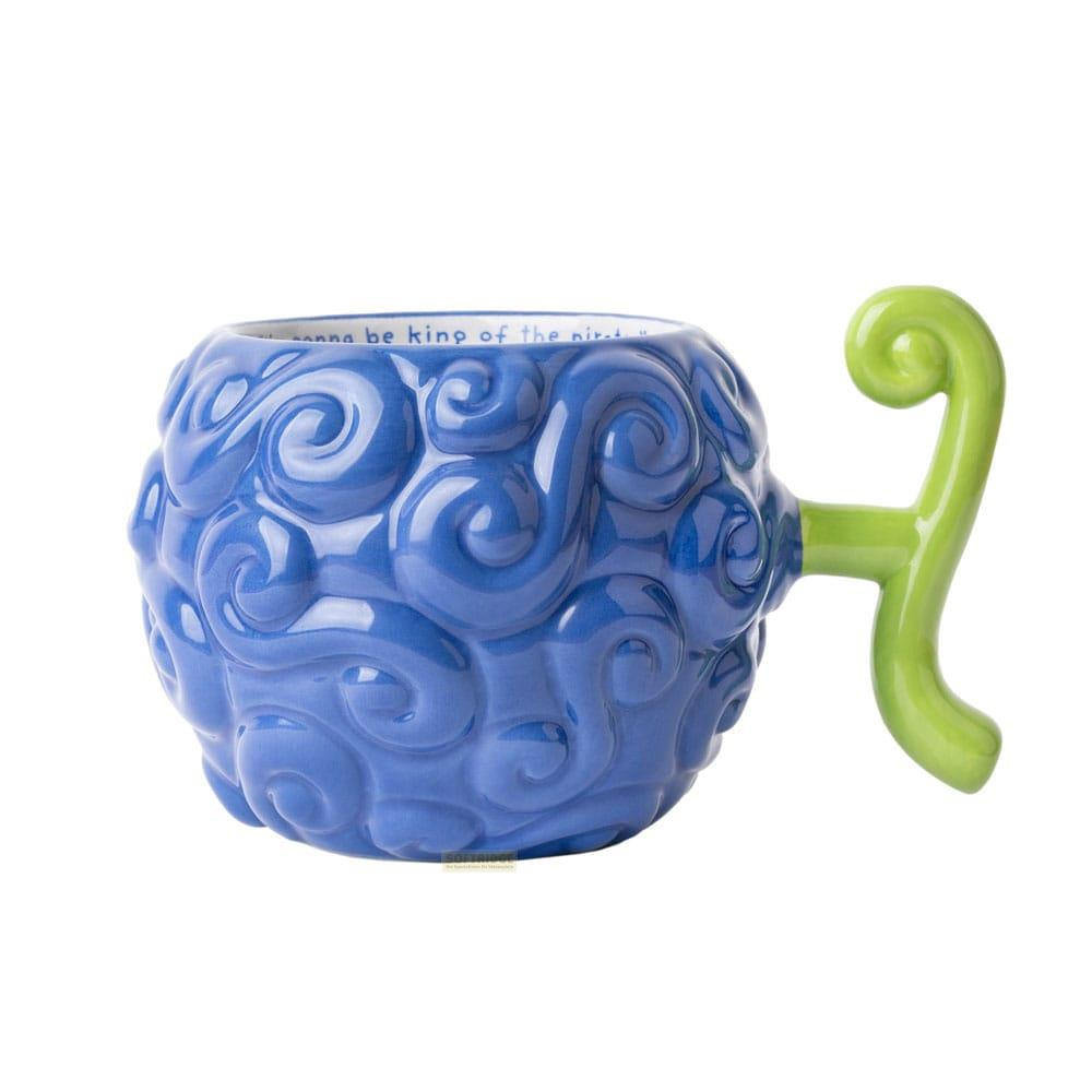 Una taza azul con forma de Fruta del Diablo, con tallo y asa verdes. Texto en el interior.