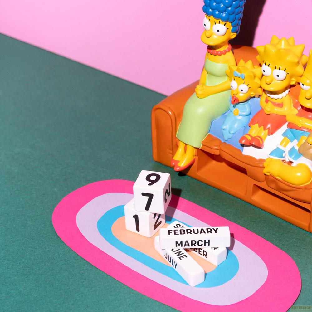 Figuras de Los Simpson en un sofá con bloques de fechas y una alfombra colorida.