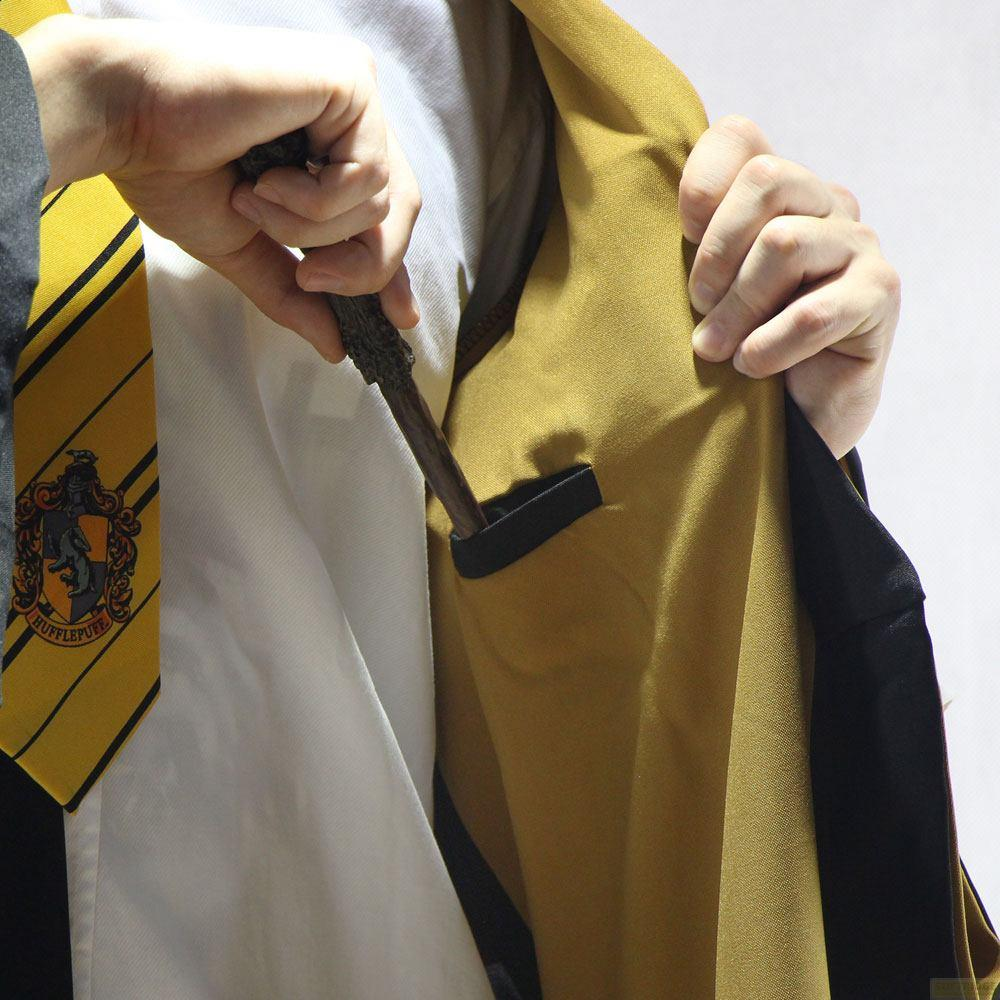 Una mano mete una varita en el bolsillo de una túnica amarilla, junto a una corbata de Hufflepuff.
