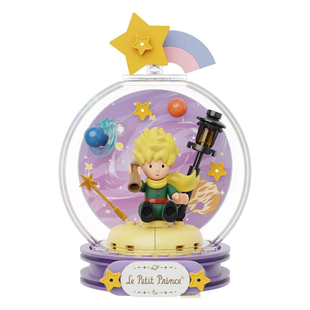 Der kleine Prinz sitzt mit Laterne in einer Glaskugel mit Sternen und einem Regenbogen.