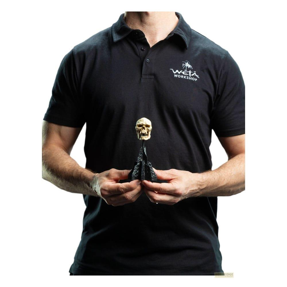 Mann in schwarzem Poloshirt hält eine kleine Totenkopf-Figur.