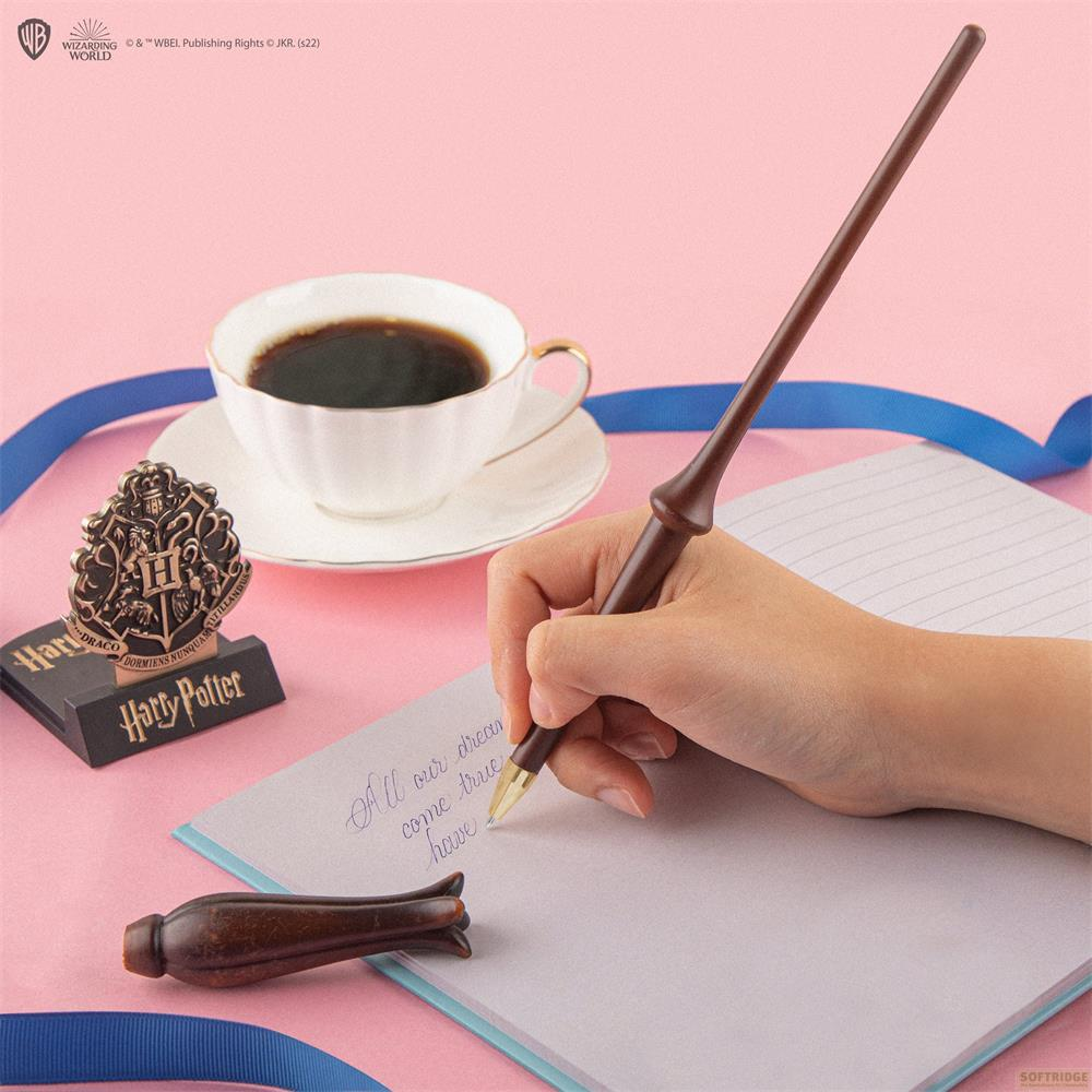 Eine Hand schreibt mit einem Zauberstabstift in ein Notizbuch. Kaffee und ein Wappen sind daneben.