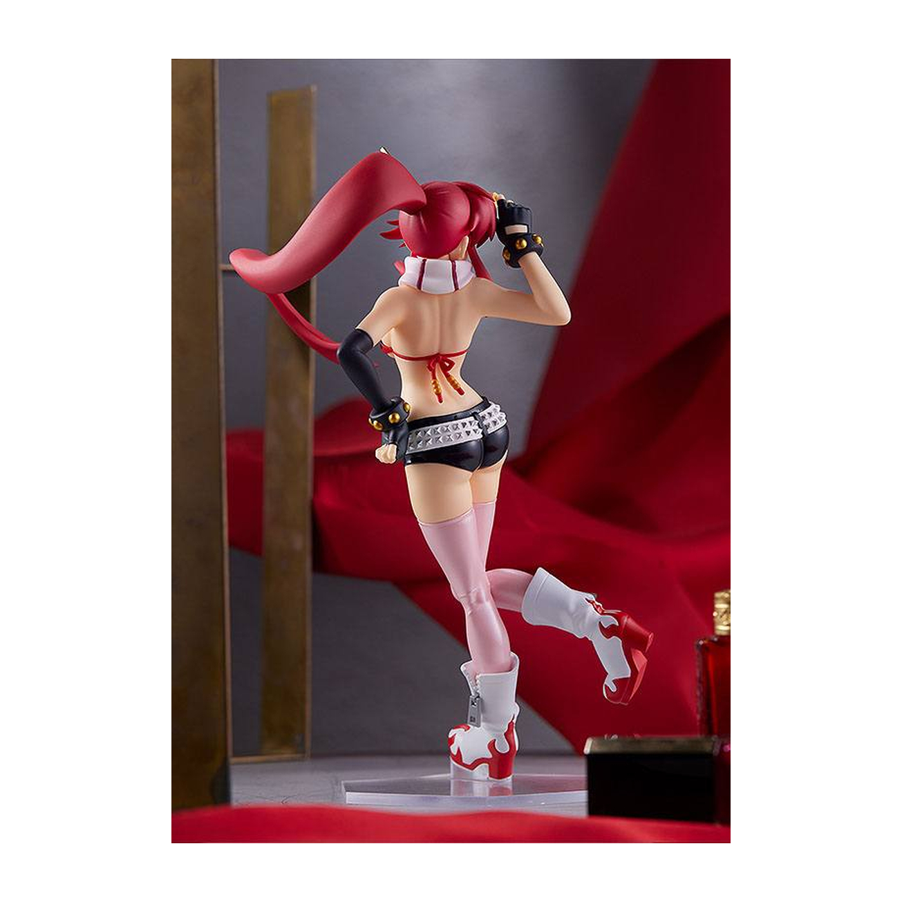 Una figura de pelo rojo, con bikini y shorts, se alza ante tela roja.