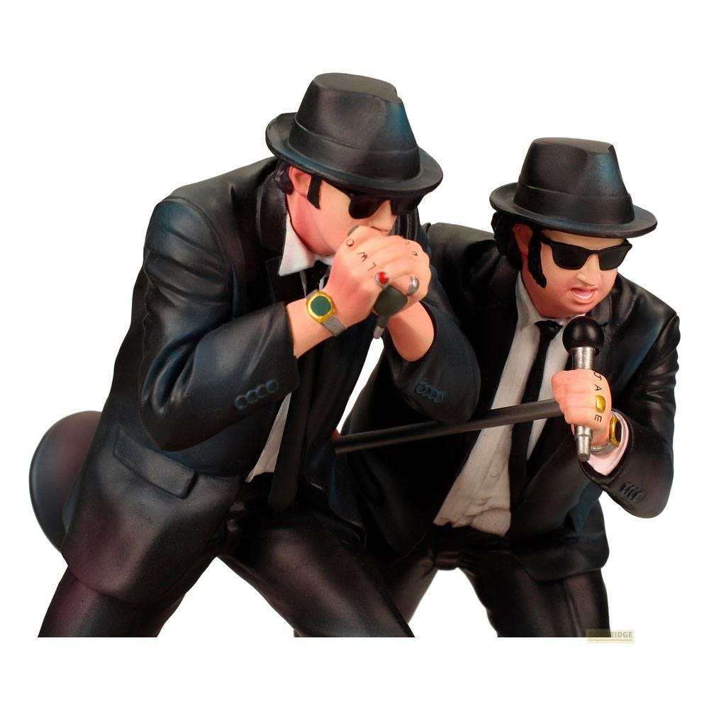 Dos figuras con trajes negros y sombreros cantan en micrófonos y armónicas.