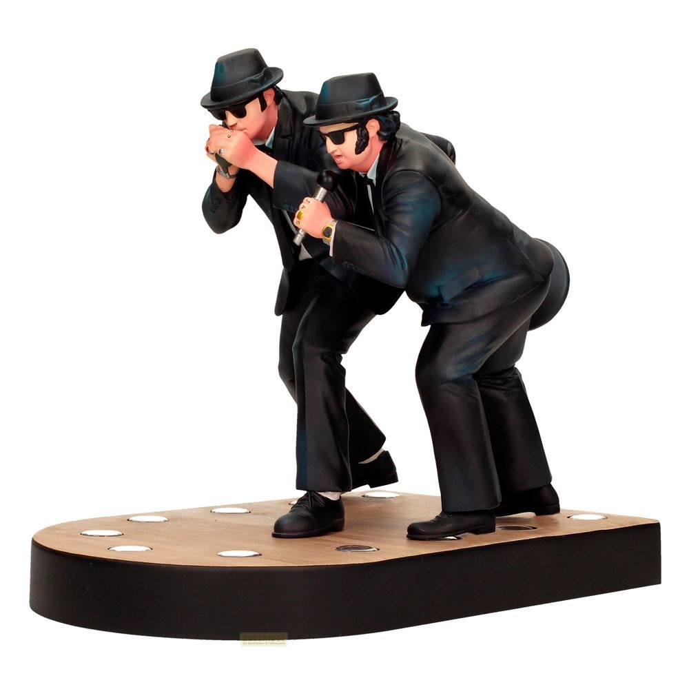 Dos figuras con trajes y sombreros negros en un escenario, uno toca armónica, el otro canta.