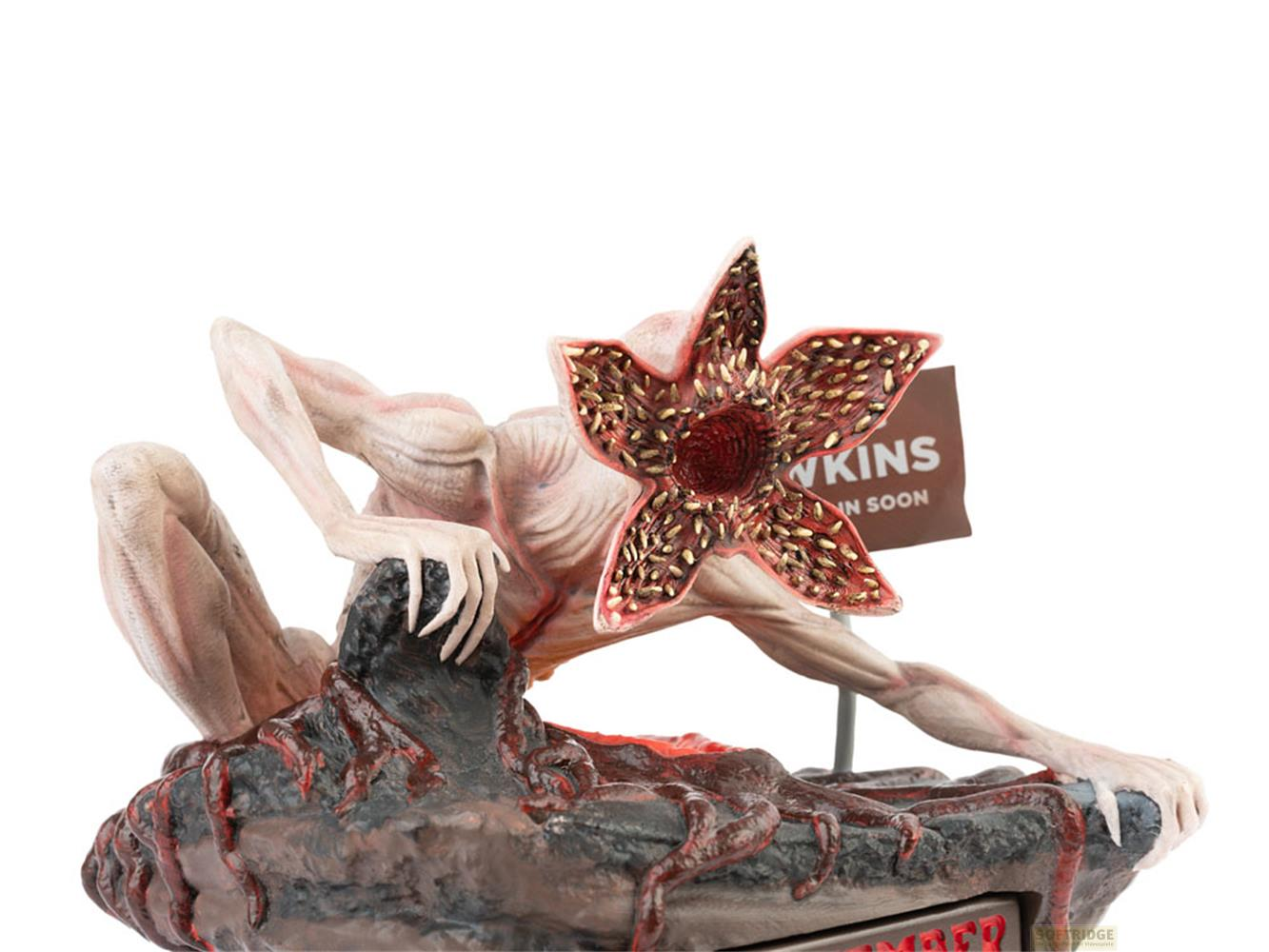 Figura de Demogorgon con boca de flor, trepando rocas. Un cartel dice "Hawkins" al fondo.