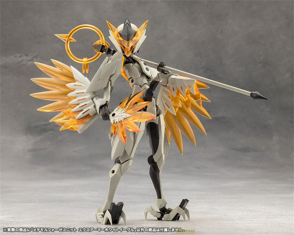 Une figurine blanche et dorée avec des ailes et une lance sur fond gris.