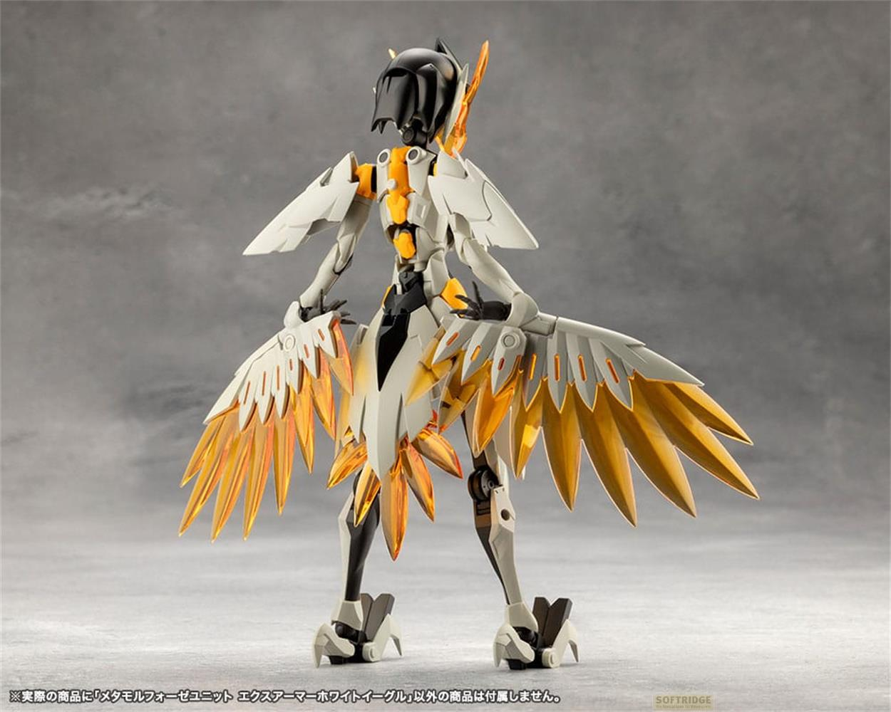 Un robot blanc et or avec des ailes se dresse sur fond gris.
