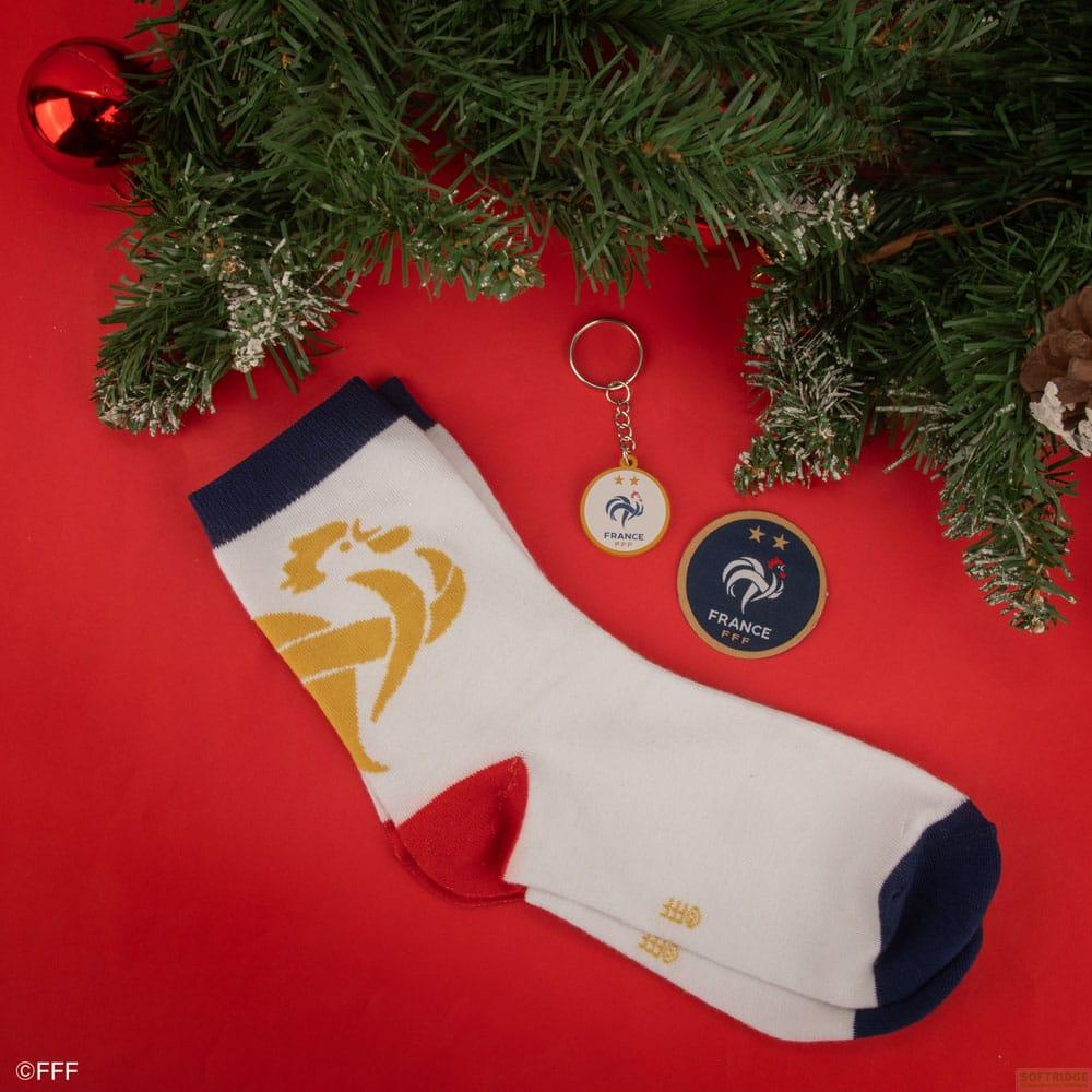 Weiße Socken, Schlüsselanhänger und Aufnäher mit Frankreich-Logo auf rotem Hintergrund mit Tannenzweigen.