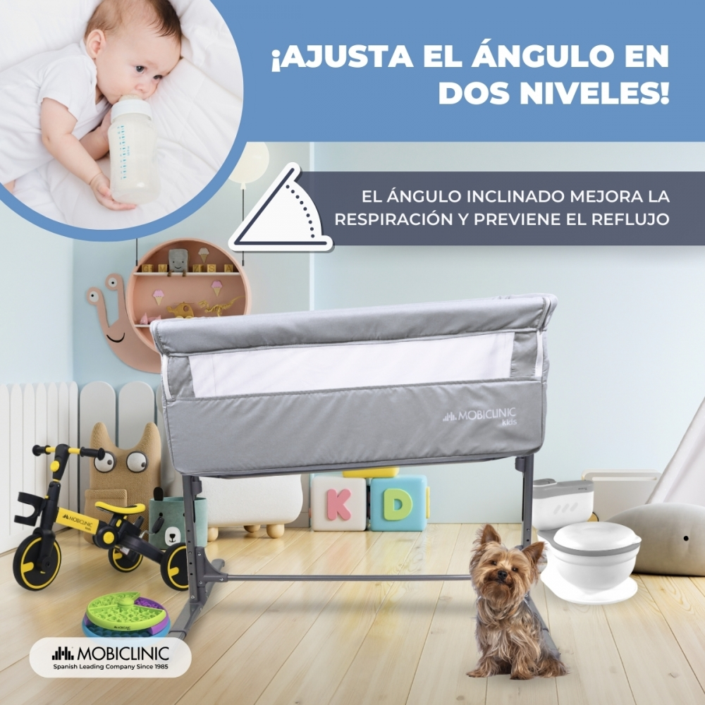 Cuna con ángulo ajustable, junto a un perro, juguetes y bloques.