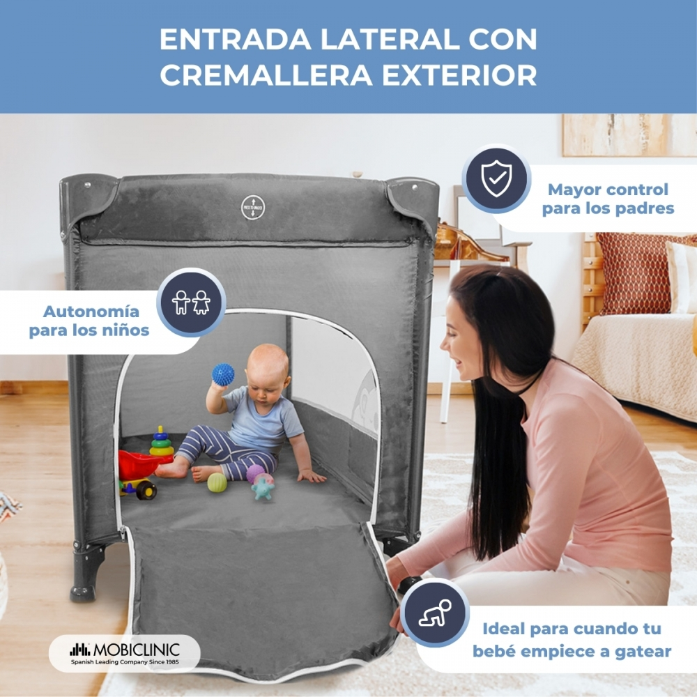 Un bebé juega en un corralito gris, observado por una mujer.