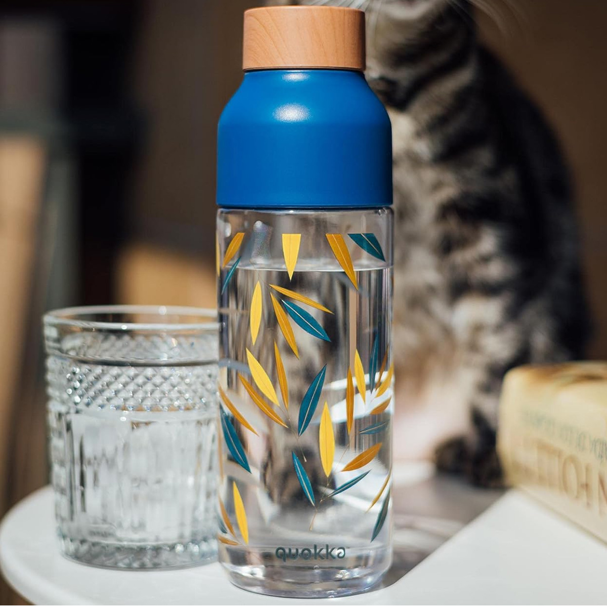 Una bottiglia di vetro con tappo blu e motivo a foglie accanto a un bicchiere.