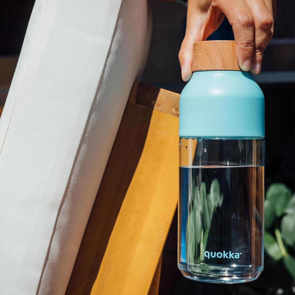 Una mano tiene una bottiglia d'acqua trasparente con tappo blu e parte superiore in legno.