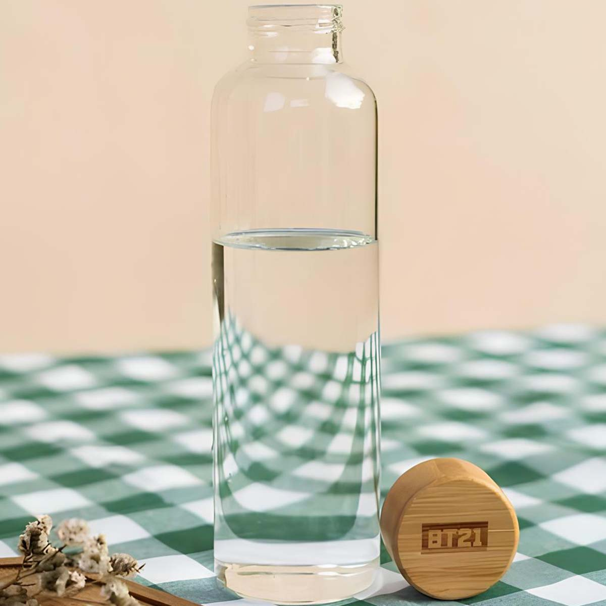 Una bottiglia di vetro con acqua si trova su una tovaglia a quadri verdi e bianchi accanto a un tappo di legno.