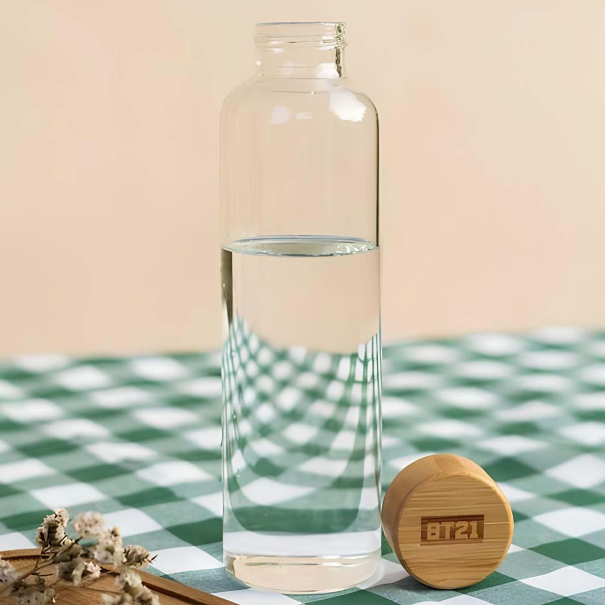 Una bottiglia di vetro con acqua su una tovaglia a scacchi verdi e bianchi.
