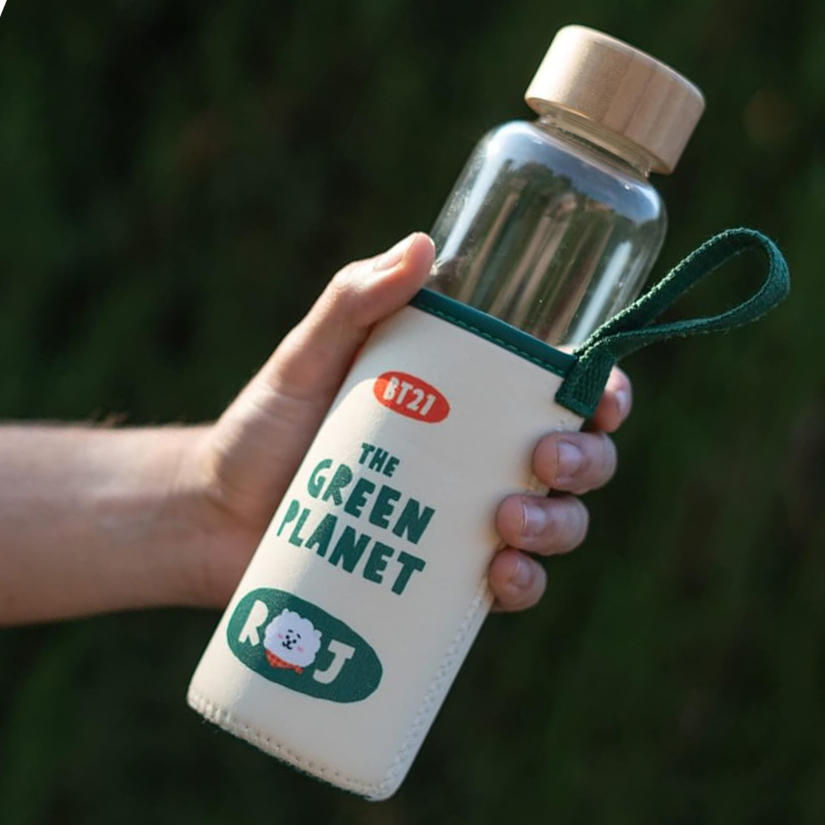 Una mano tiene una borraccia BT21 "The Green Planet" con coperchio in legno.
