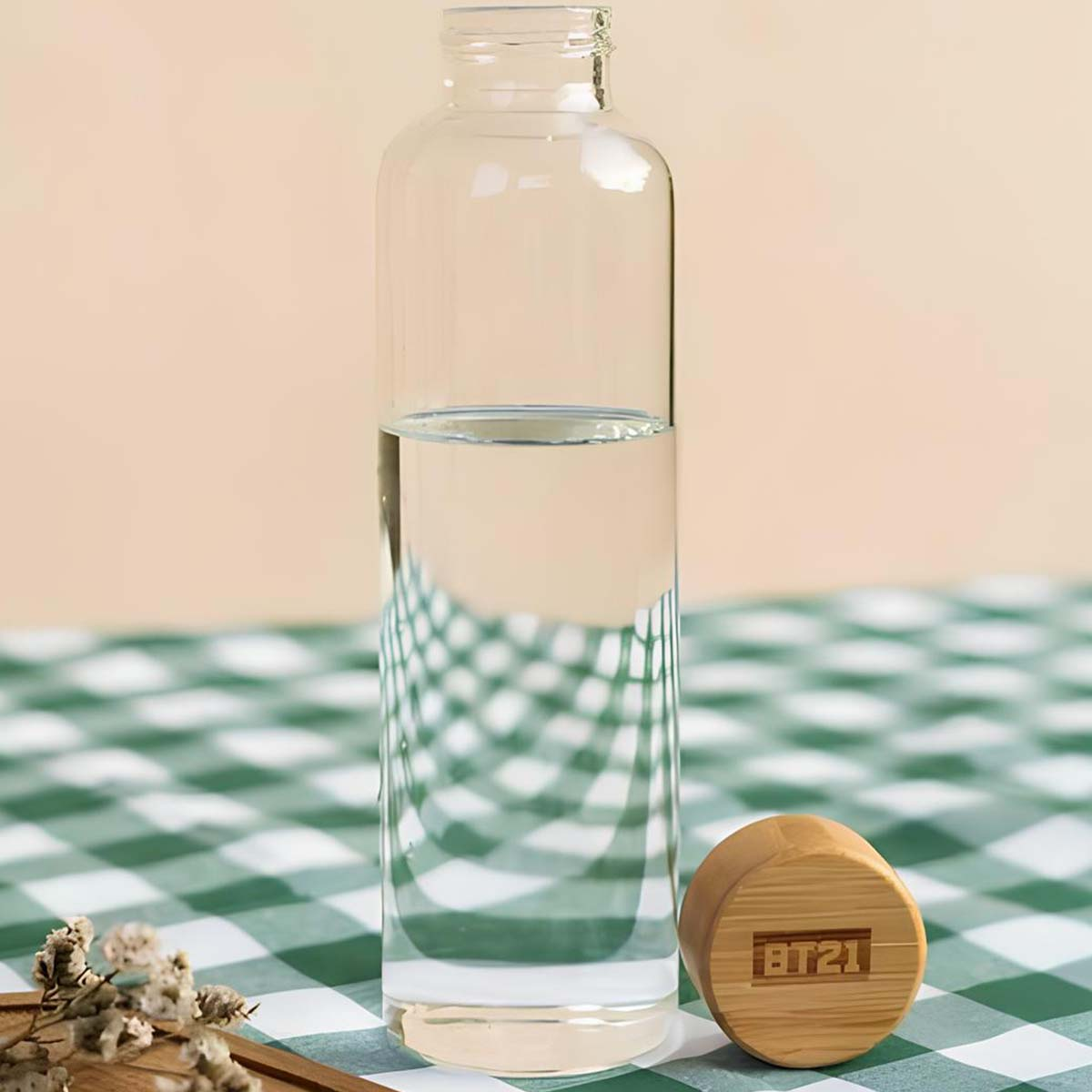 Bottiglia di vetro mezza piena d'acqua su telo a quadri verdi, tappo BT21.
