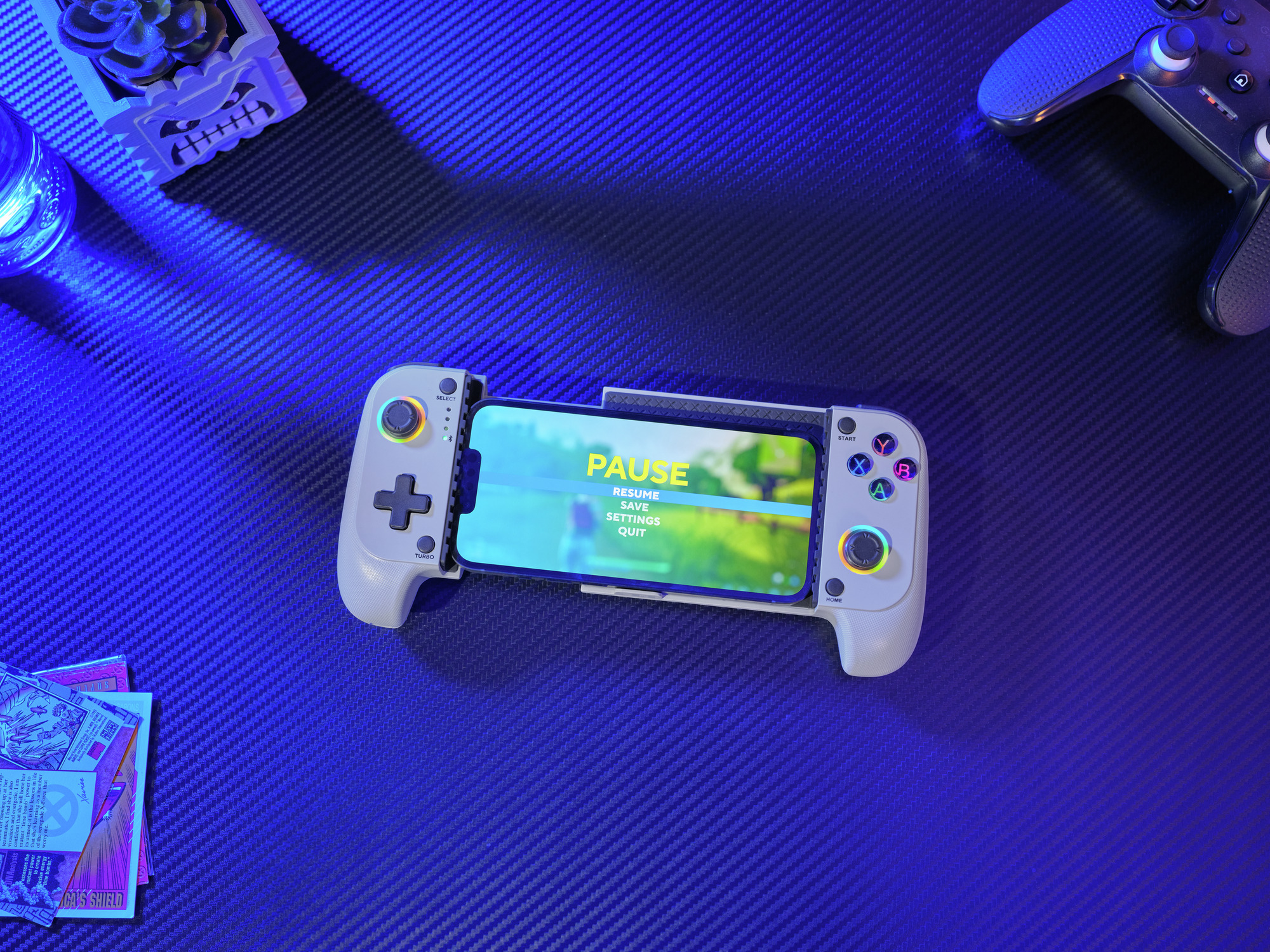 Ein Smartphone mit einem PAUSE-Menü ist in einen weißen Controller eingebettet, daneben liegen Controller.
