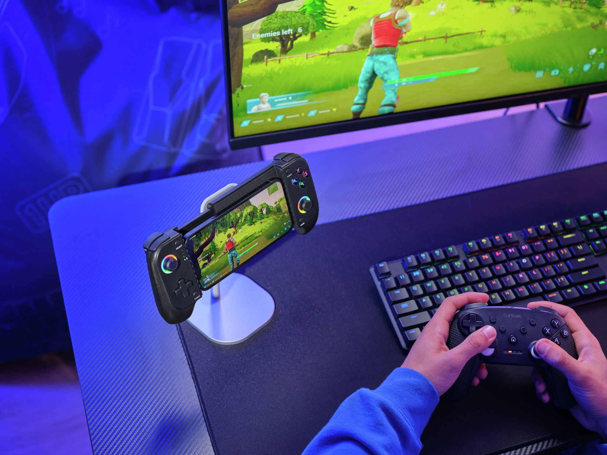Osoba gra w grę wideo z kontrolerem i telefonem na biurku.