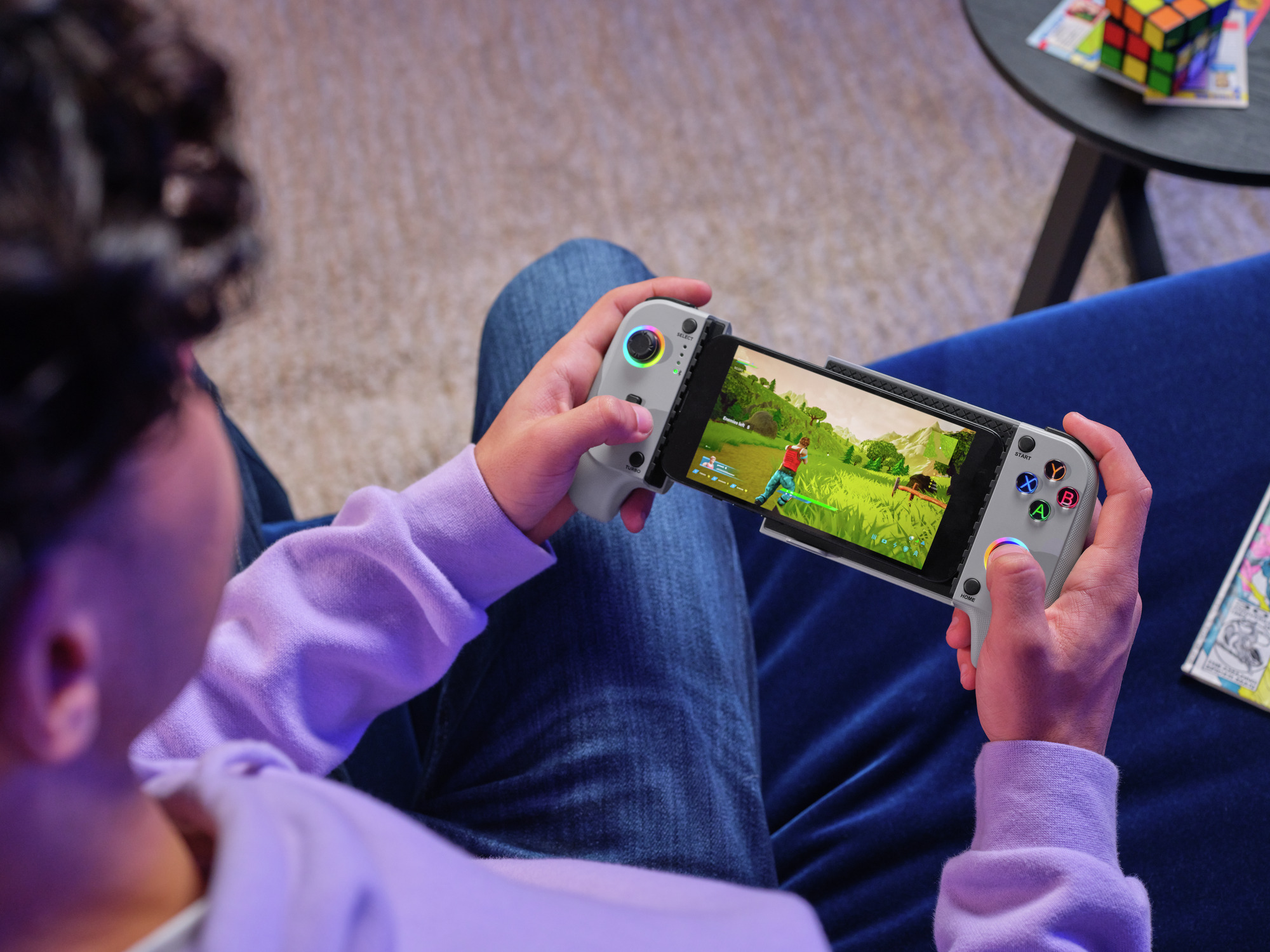 Person spielt ein Videospiel auf einem Handheld-Gerät mit bunten Grafiken. Das Gerät hat graue Controller.