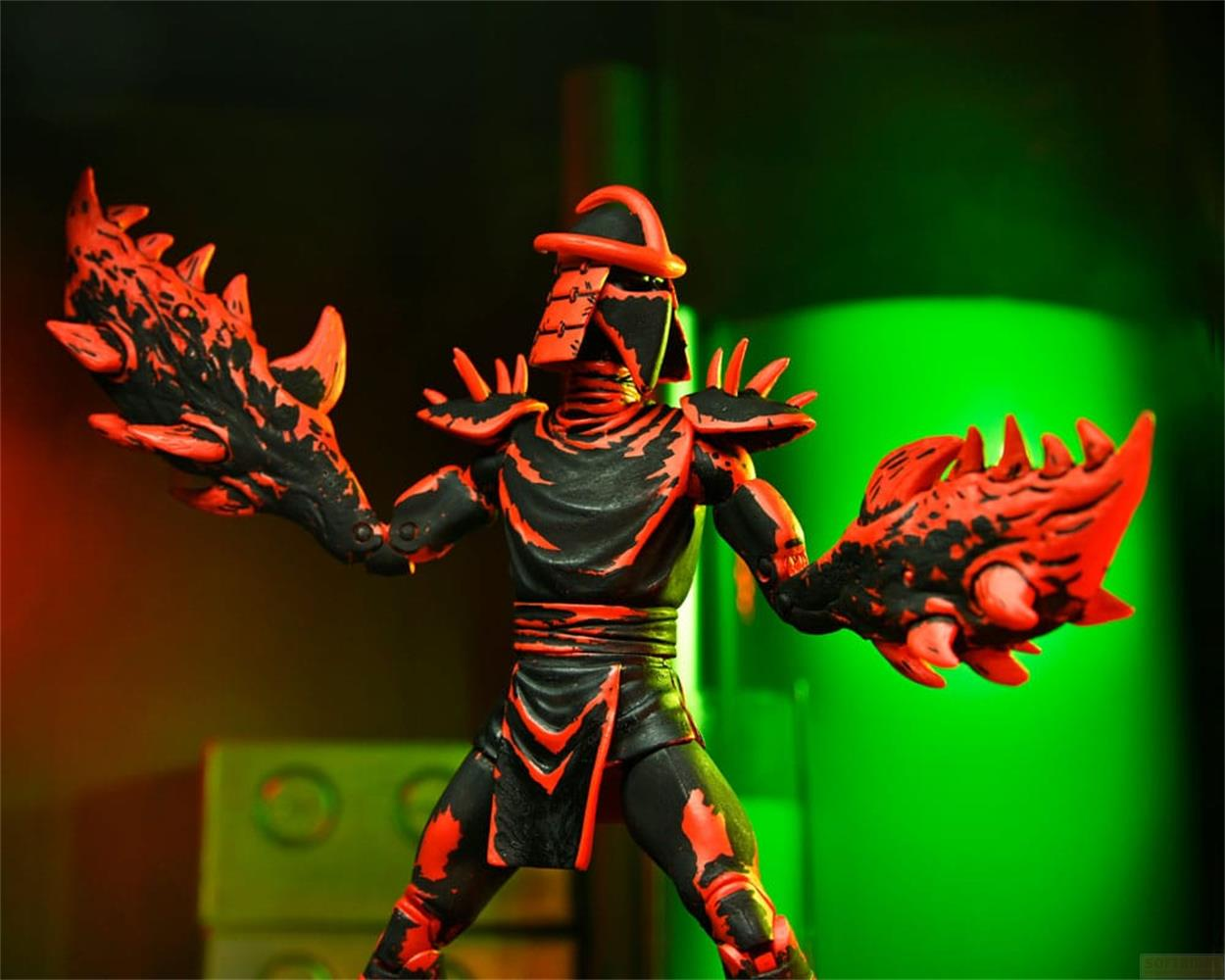 Una figura de acción negra y roja con armas de garra, sobre fondo verde.