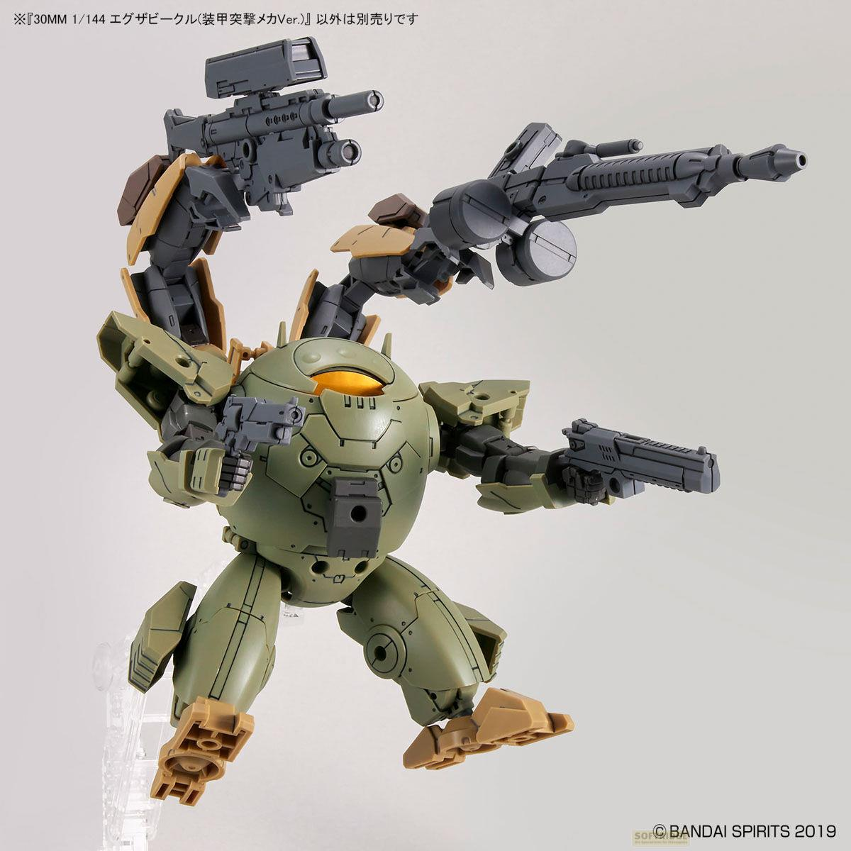 Grüne und beige Mech-Figur mit Waffen, die auf einem Ständer steht.