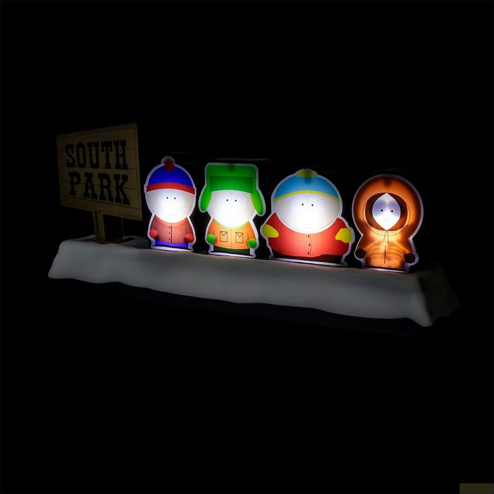 Vier beleuchtete South Park Figuren stehen vor einem Schild auf dunklem Hintergrund.