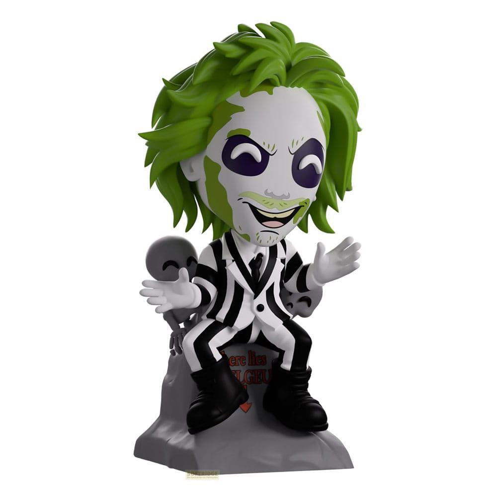 Eine Figur von Beetlejuice mit grünem Haar, weißem Gesicht, gestreiftem Anzug auf einem Grabstein.