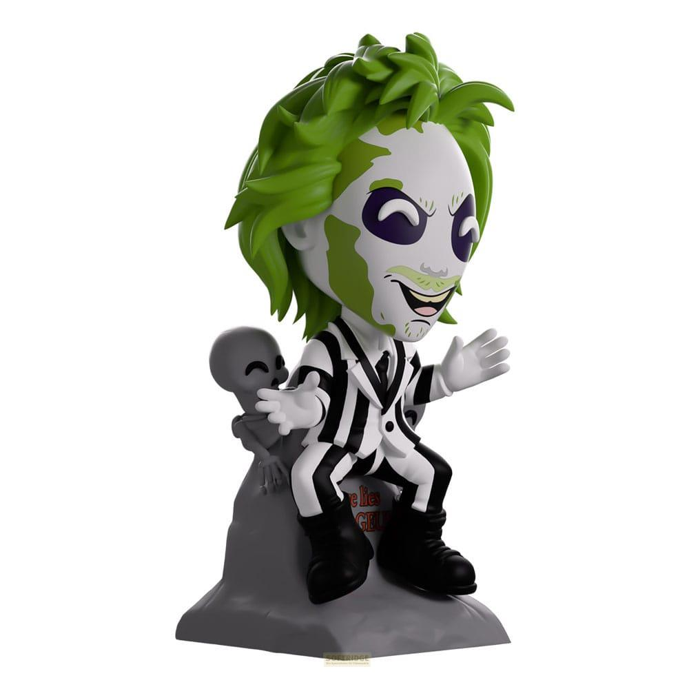 Beetlejuice-Figur mit grünem Haar, schwarz-weißer Anzug, sitzt auf Grabstein mit Skelett.