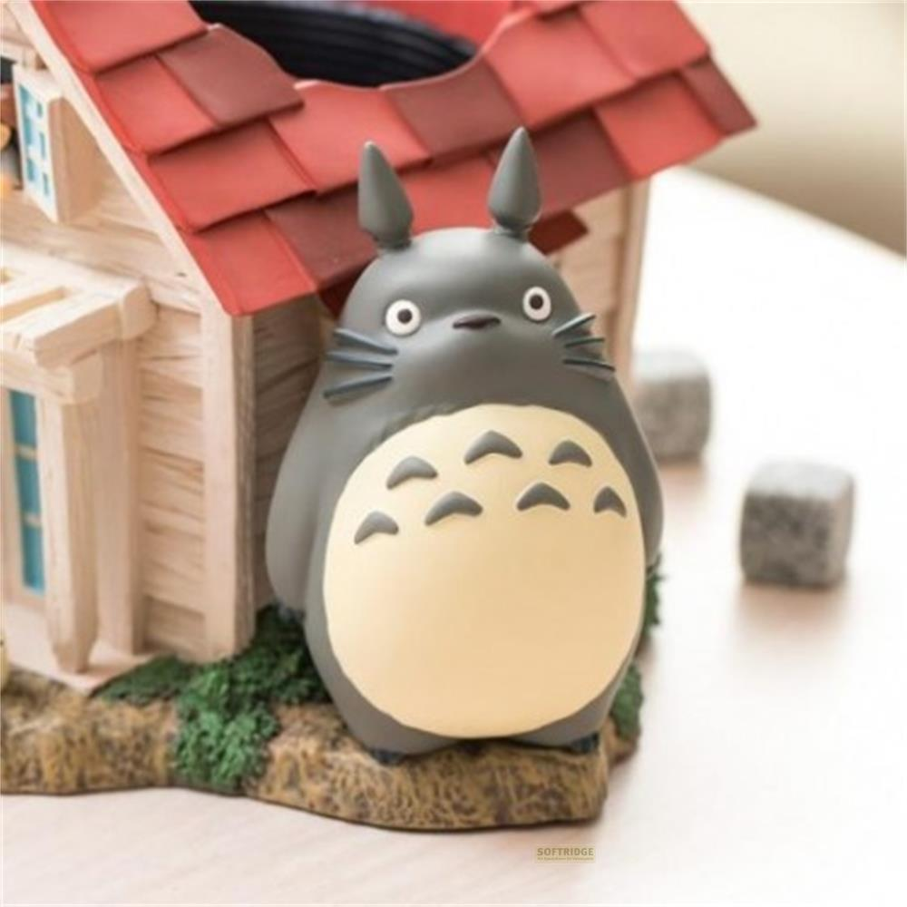 Figurine de Totoro à côté d'une maisonnette au toit rouge et buissons.