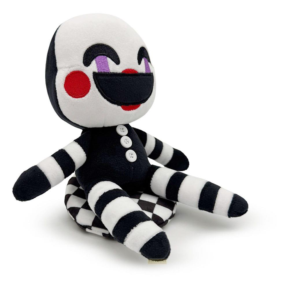 Marionnette en peluche rayée noir et blanc assise sur un coussin à carreaux.