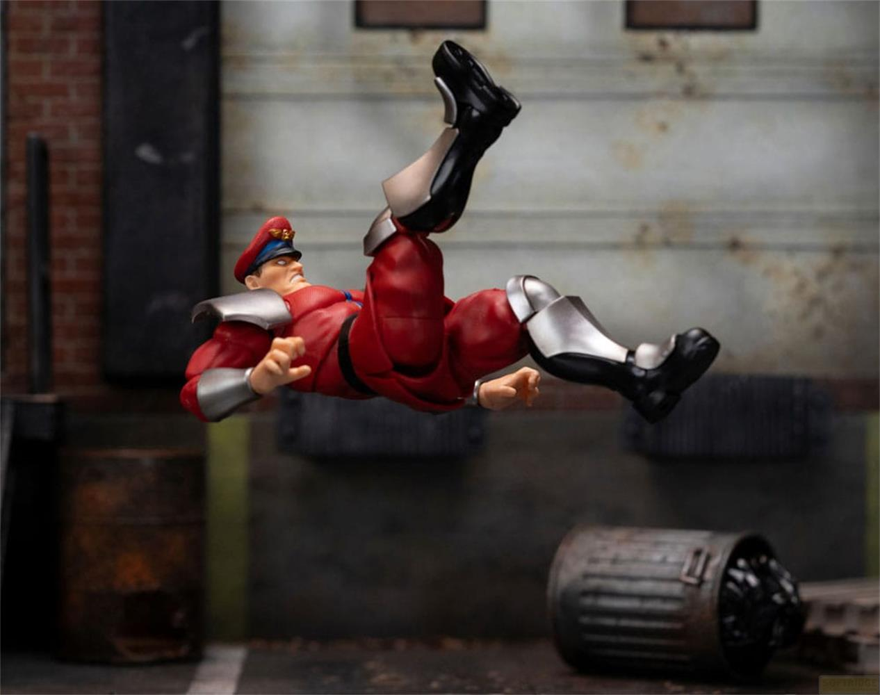 Eine Actionfigur von M. Bison fliegt durch die Luft vor einer Ziegelwand.