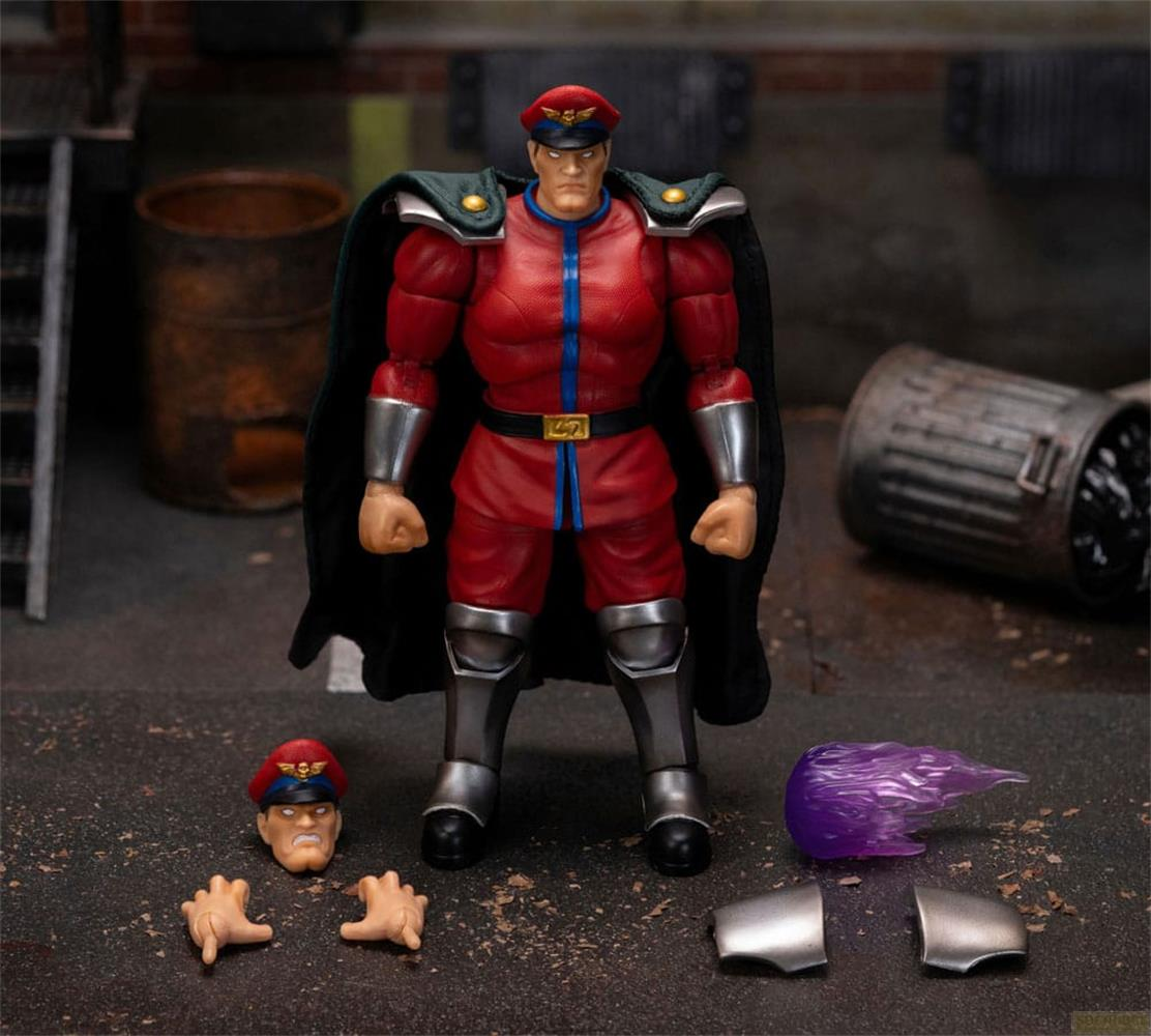 Actionfigur von M. Bison in Rot mit schwarzem Umhang, Zubehör auf dem Boden.