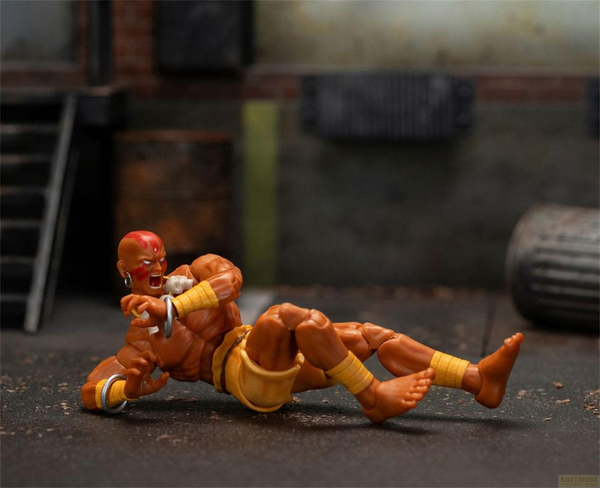 Una action figure di uomo con pelle arancione e segno rosso sulla testa giace a terra.