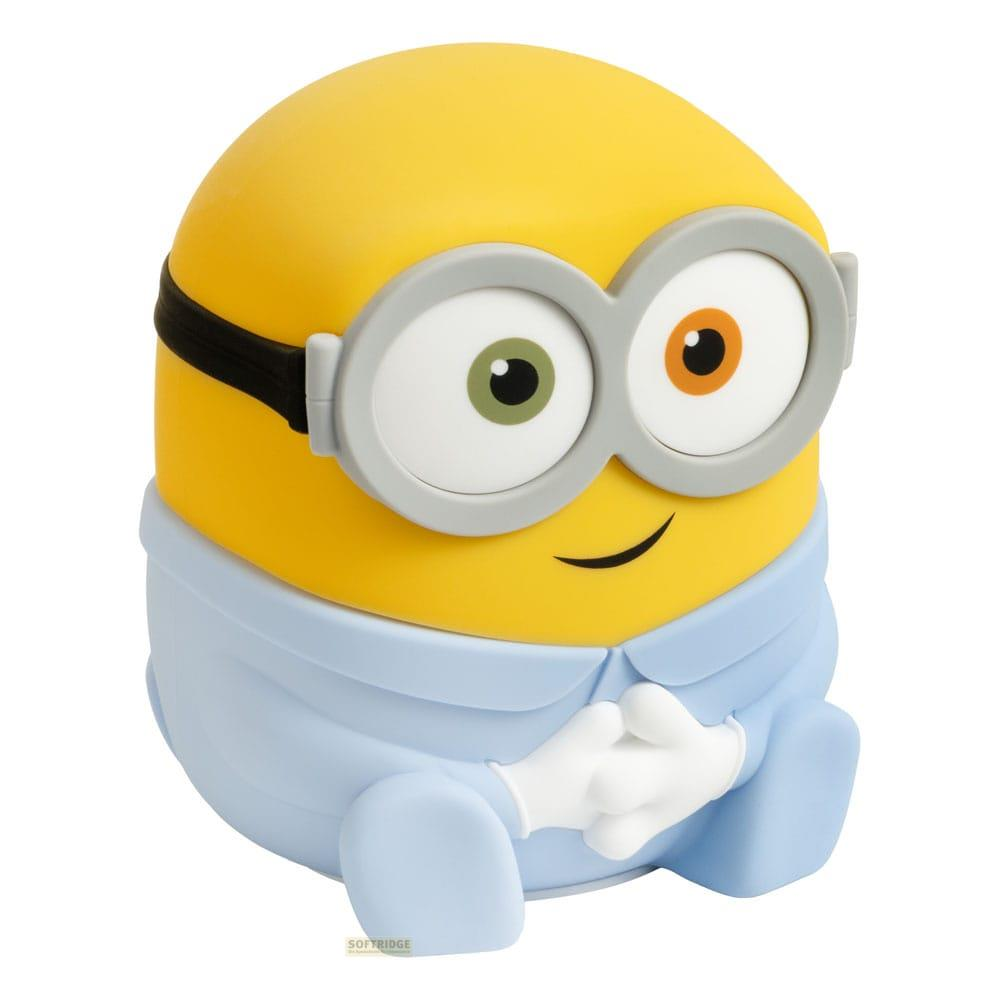 Żółty minion w niebieskich ogrodniczkach, goglach, siedzi ze złożonymi rękami.