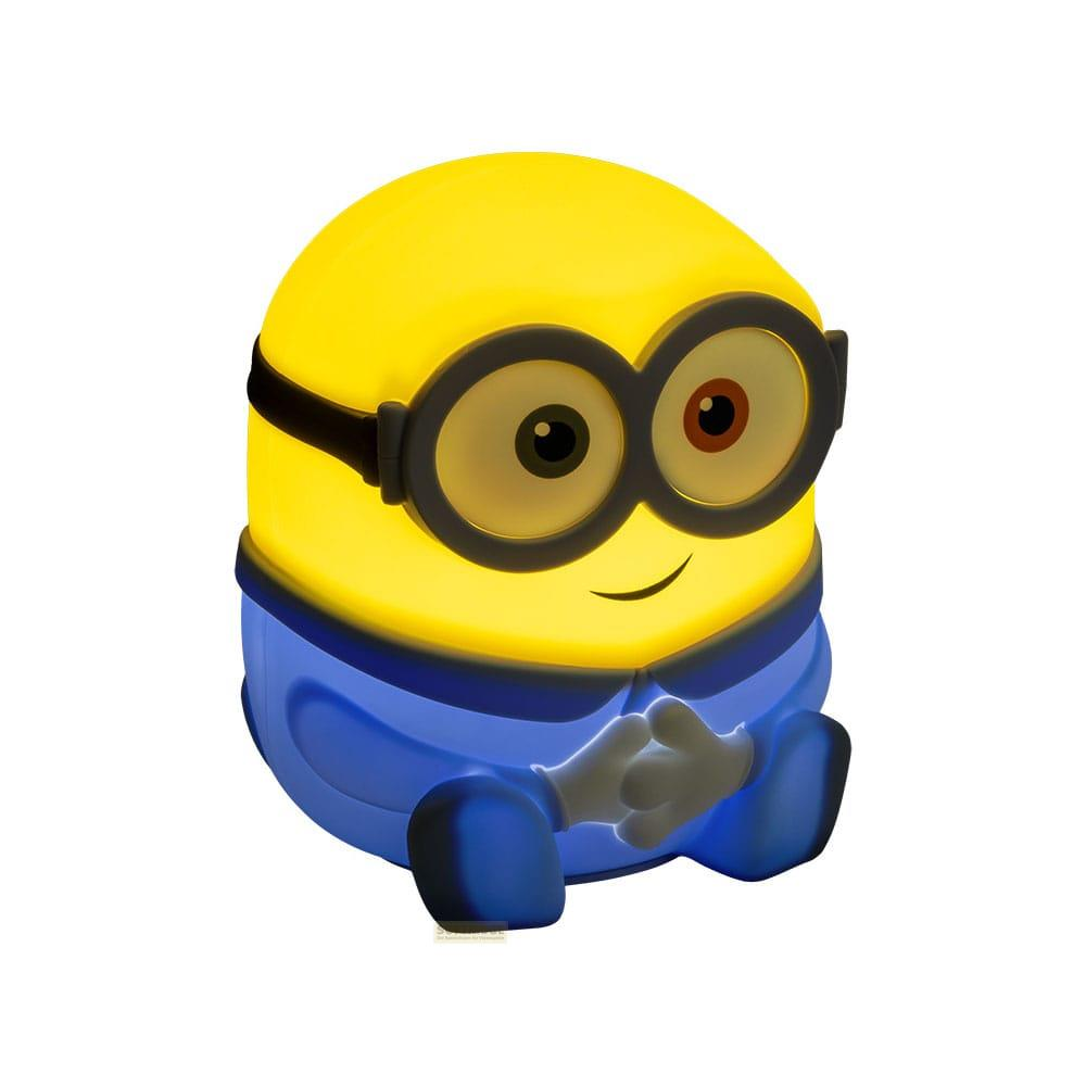 Żółta lampka Minion w niebieskich ogrodniczkach, siedząca na podłodze.
