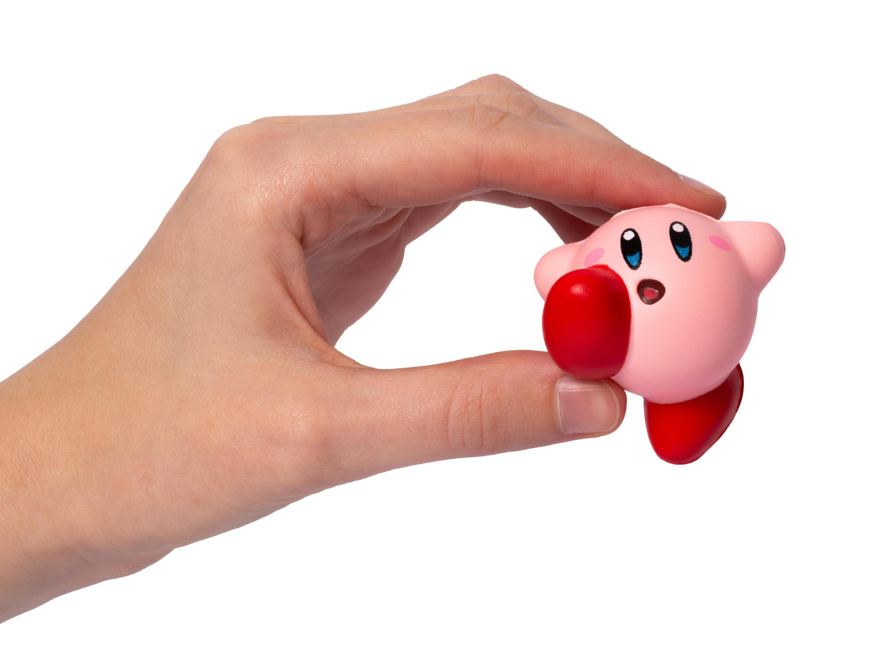 Une main tient une petite figurine rose de Kirby avec des joues et des pieds rouges.