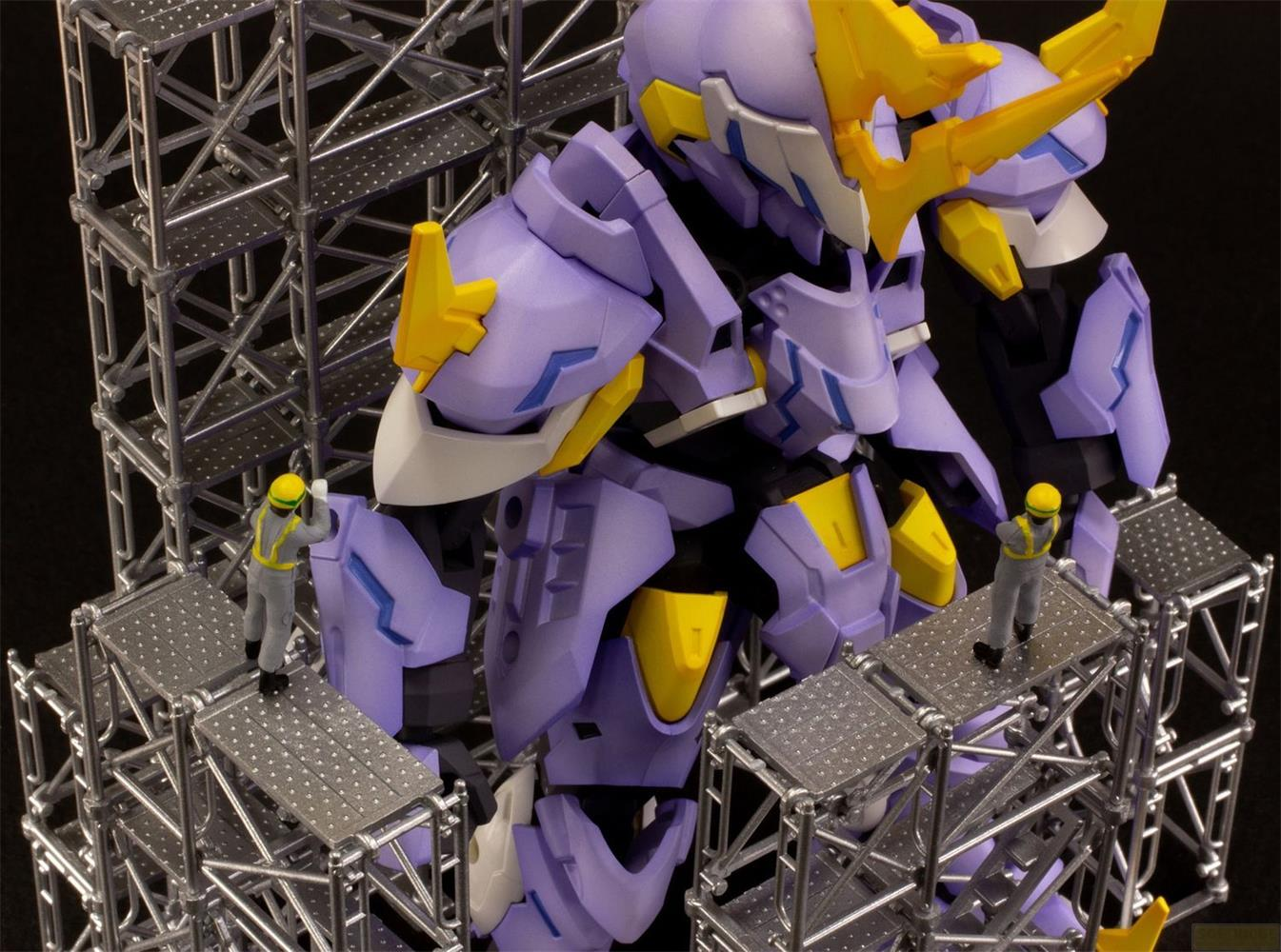 Un robot violet aux accents jaunes sur échafaudage avec de petites figurines.