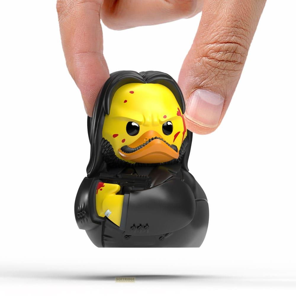 Un pato de goma amarillo con pelo y traje negros, sosteniendo un arma.