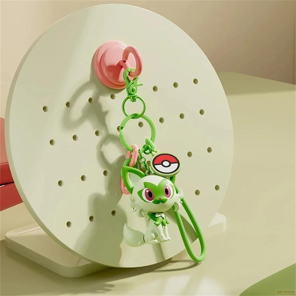 Un porte-clés Pokémon chat vert et blanc pend d'un crochet rose sur un panneau perforé.