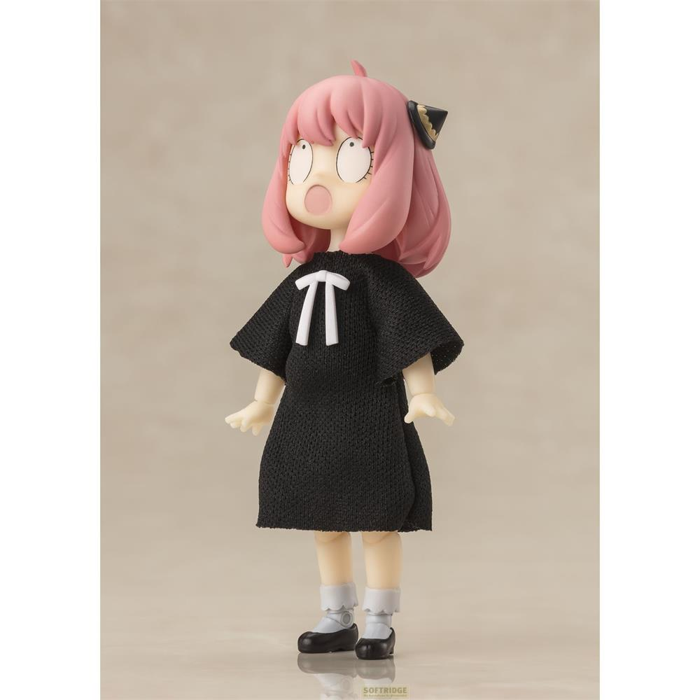 Una figura con capelli rosa indossa un vestito nero con un simbolo bianco.