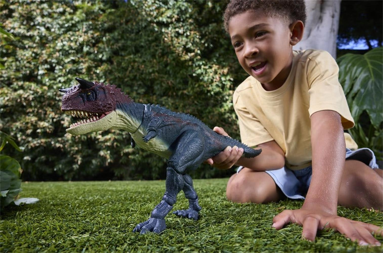 Un niño con camiseta amarilla juega con un juguete de dinosaurio sobre césped verde.