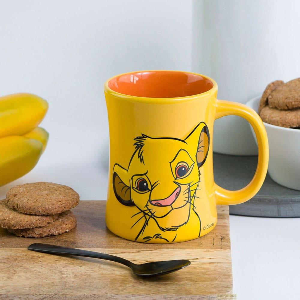 Taza amarilla con diseño de Simba, junto a plátanos, galletas y una cuchara.