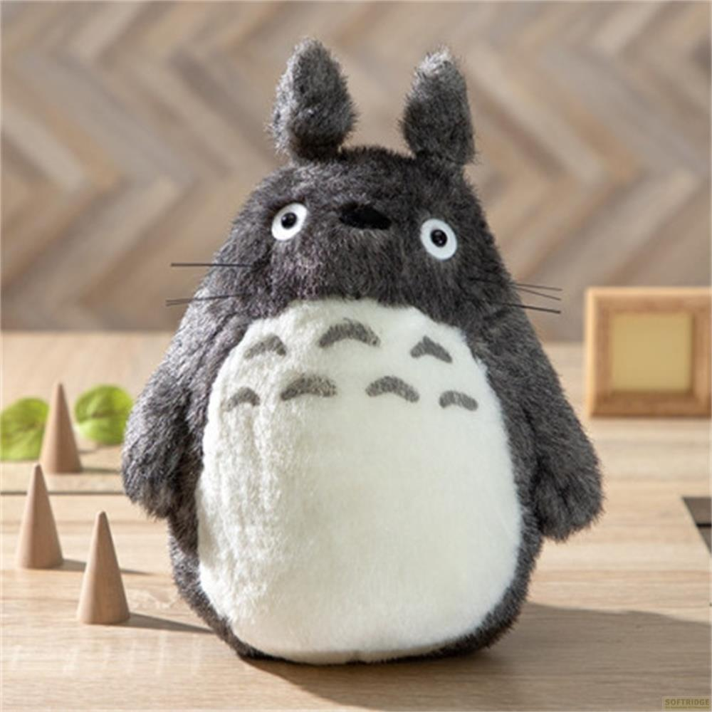 Un morbido peluche grigio di Totoro su un tavolo di legno con decorazioni.