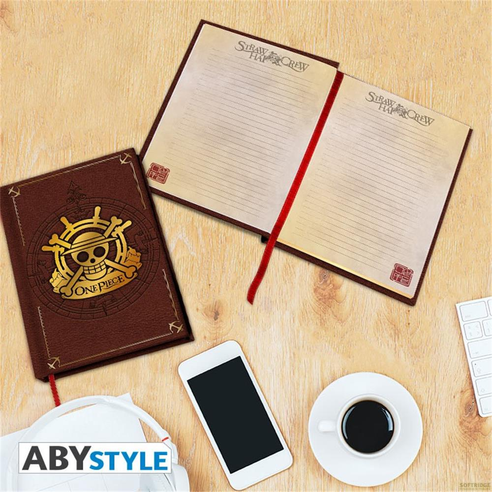 Un carnet marron One Piece, un carnet ouvert, un smartphone et du café sur un bureau.