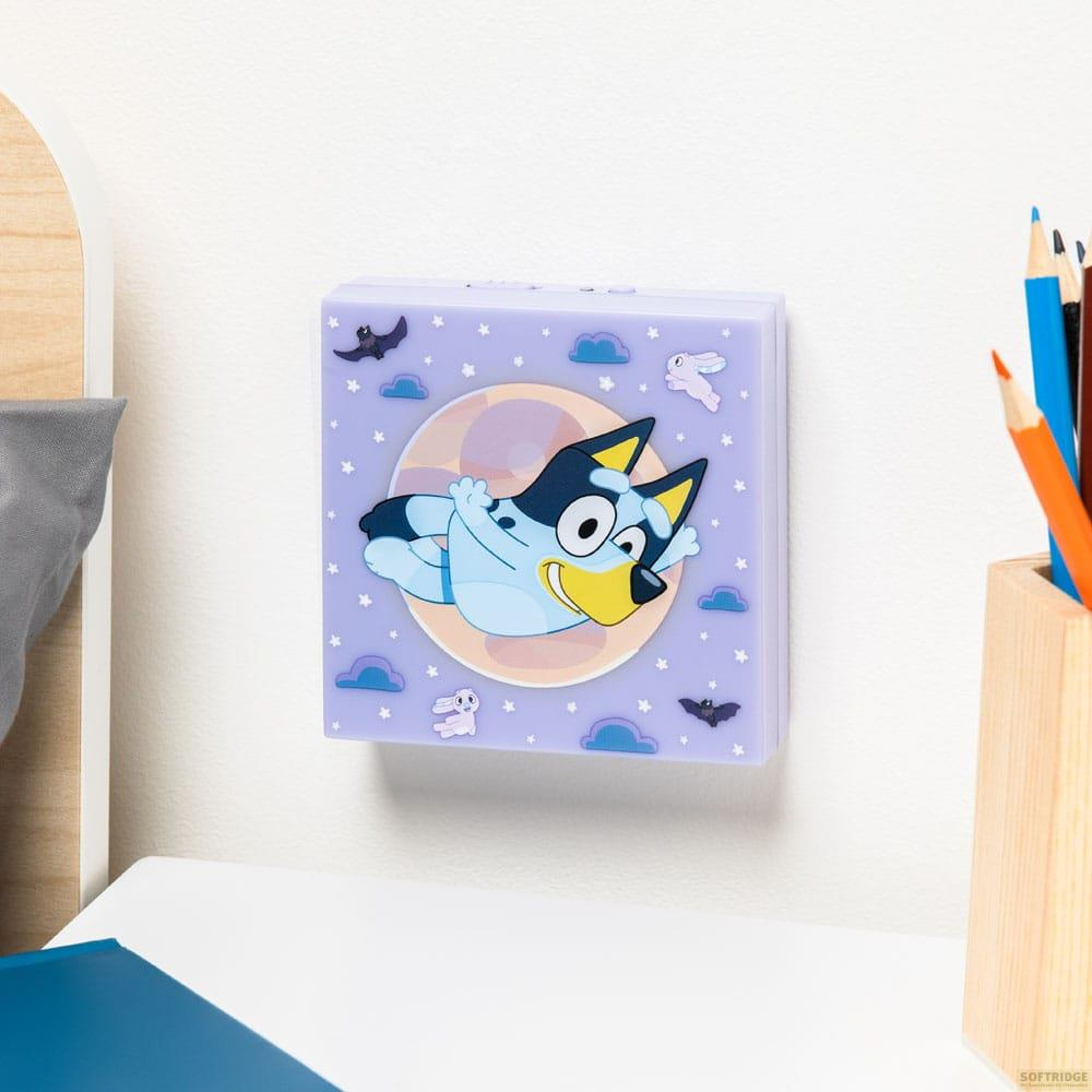 Bluey leci przed księżycem z małymi chmurami, gwiazdami i nietoperzami na fioletowym tle.